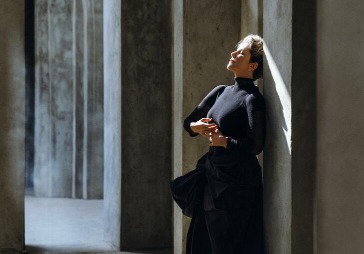 Joyce DiDonato in a black dress, leaning with her back against a wall