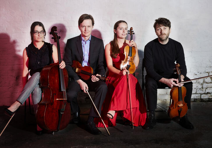 The Ligeti Quartet sitting in a row, holding their instruments