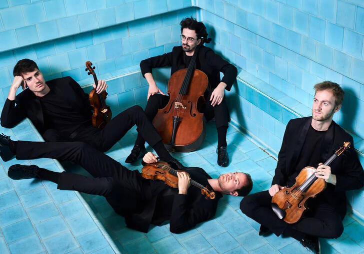 The four members of Quatuor Agate in black suits, sitting in various positions in an empty swimming pool, holding their instruments