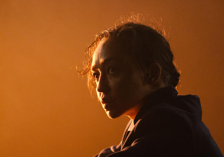 Actor Ruth Negga stares thoughtfully off-camera as a golden glow lights the stage behind her. 