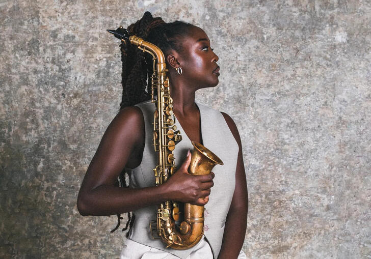 A profile shot of Cassie Kinoshi holding her saxophone in front of a concrete wall