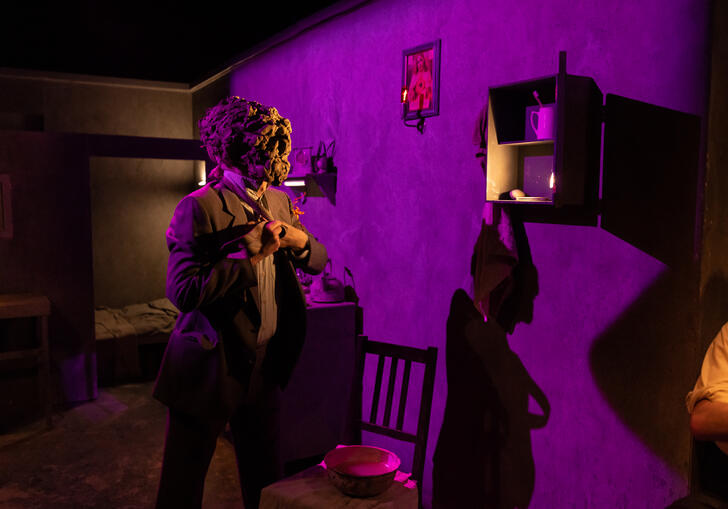 A person in a suit wearing a clay mask gets dressed.