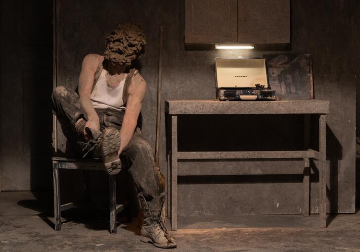 A person with a clay mask on their face sits on a chair and takes off their boots,