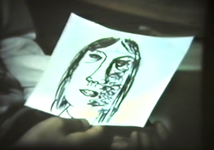 A hand holds a piece of paper with a face drawn on it. 