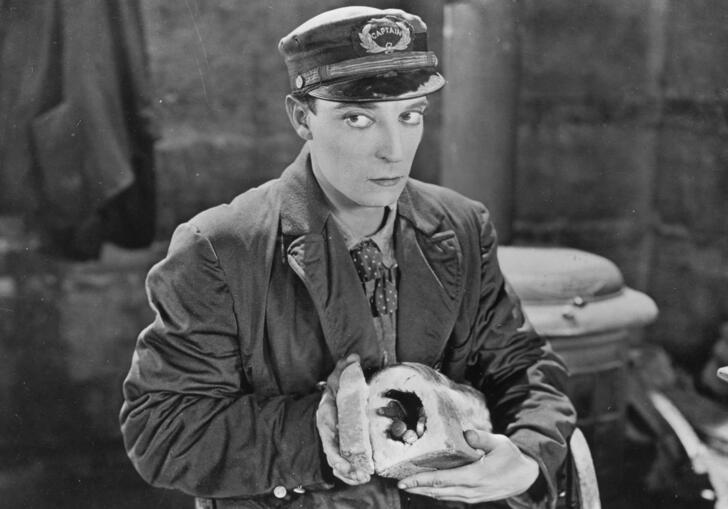 A black and white image of a man dressed in a cap and holding a hollowed out loaf of bread.