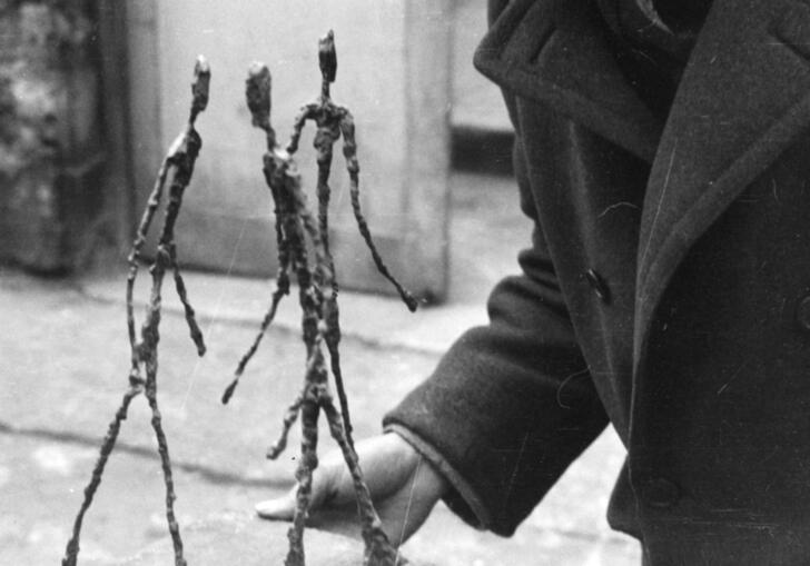 A black and white photo of Alberto Giacometti in his studio holding his sculpture, Three Men Walking.