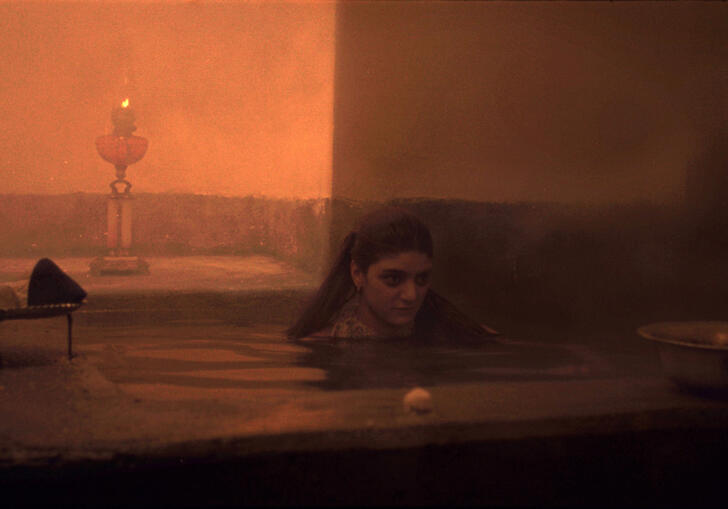 A still from Chess of the Wind, showing a misty, orange-hued scene of a woman in a bath.