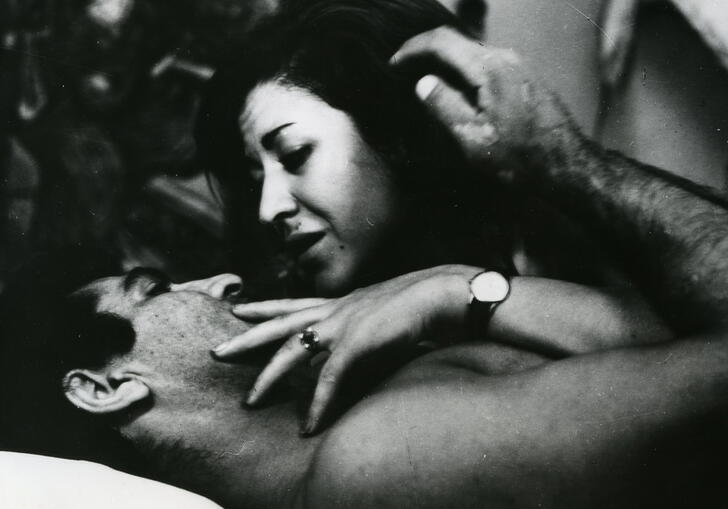 A black and white still from Brick and Mirror, showing a man and woman embracing in bed 