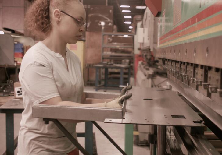 A worker holds a piece of metal against a machine. 