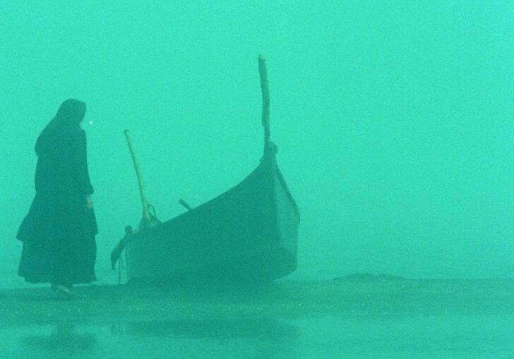 A misty scene with a bright green tint, showing a woman standing next to a moored boat.