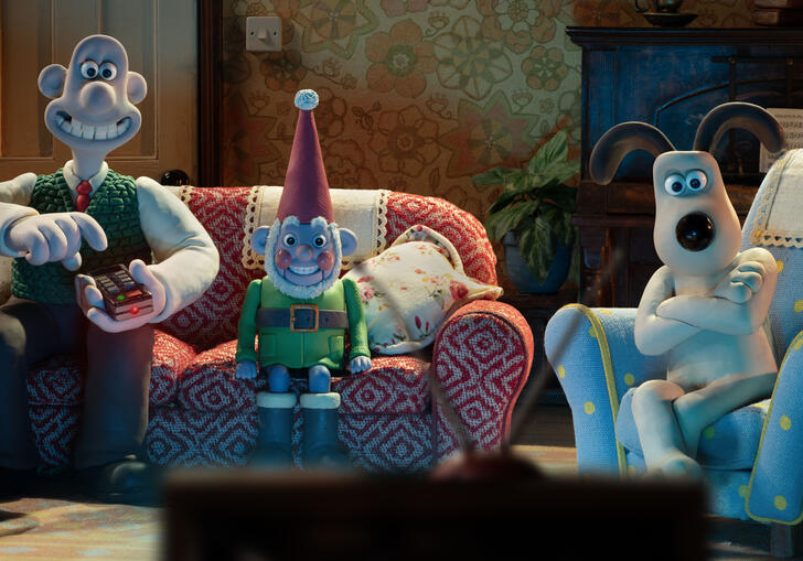 Wallace and Gromit sit on sofas with a gnome