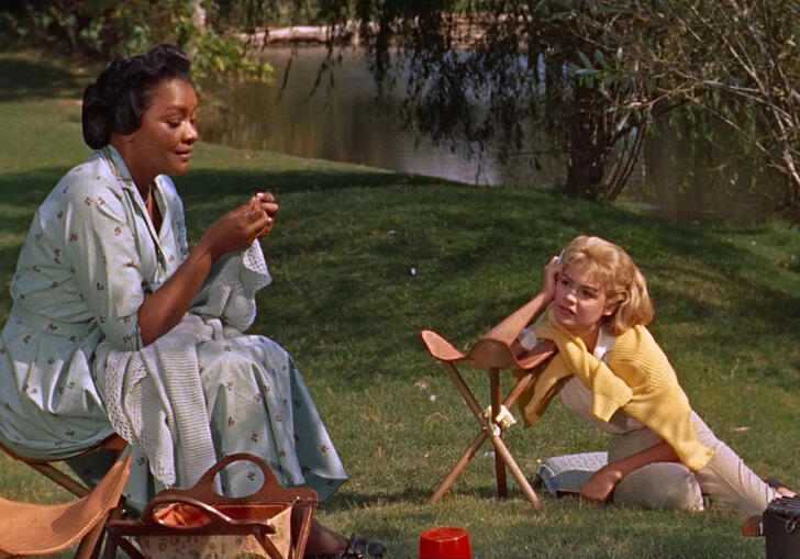 An older woman sits on the grass with a younger woman at her feet.