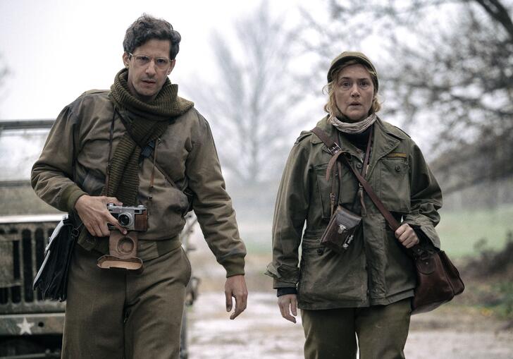 Two people in US Army fatigues walk down a road with cameras around their necks.