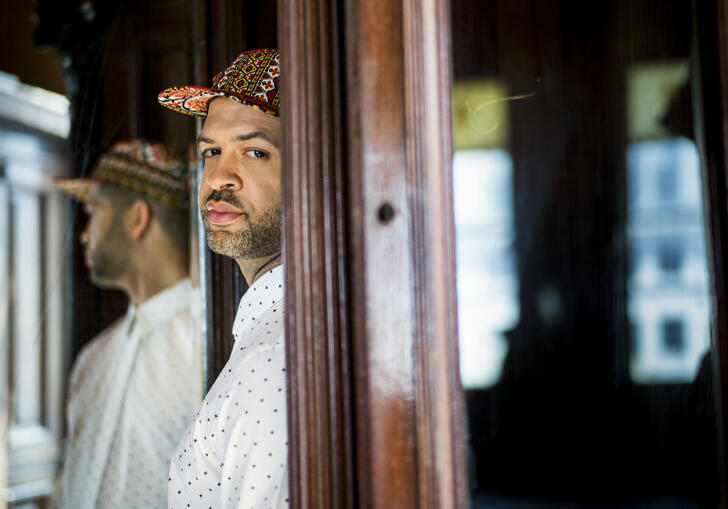 Jason Moran standing in a doorway. The back half of his body is obscured by the door frame, and he is turning to face the camera. His reflection is visible in a mirror behind him.