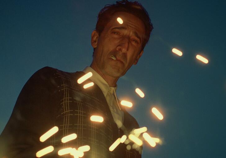 Adrien Brody stares down into camera, smoking