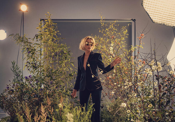 Cate Blanchett poses wearing silver sunglasses while standing in amongst flowers and lights.