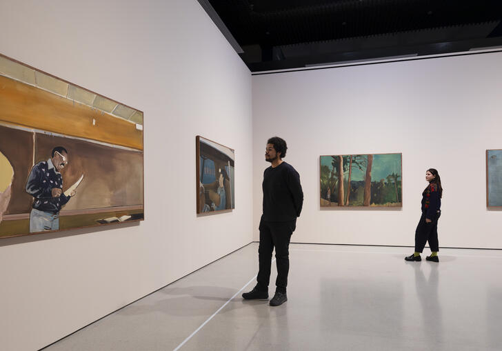 Four of Noah Davis's paintings hanging on white walls. Two people stand between the paintings, looking at them.