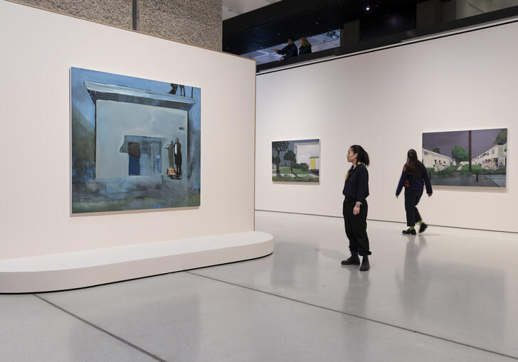 Three of Noah Davis's paintings hanging on white walls. Two people are looking at the paintings.