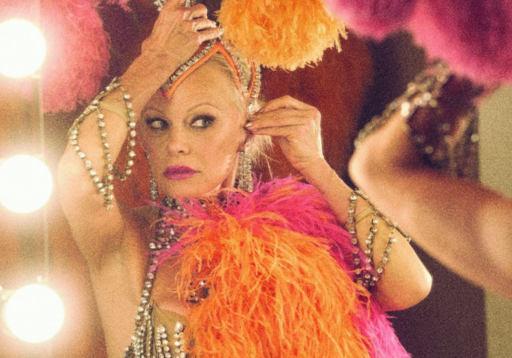 Pamela Anderson adjusts her pink and orange Las Vegas headdress in a mirror