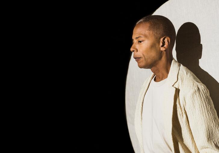 Jeff Mills under a spotlight wearing a white blazer and tshirt