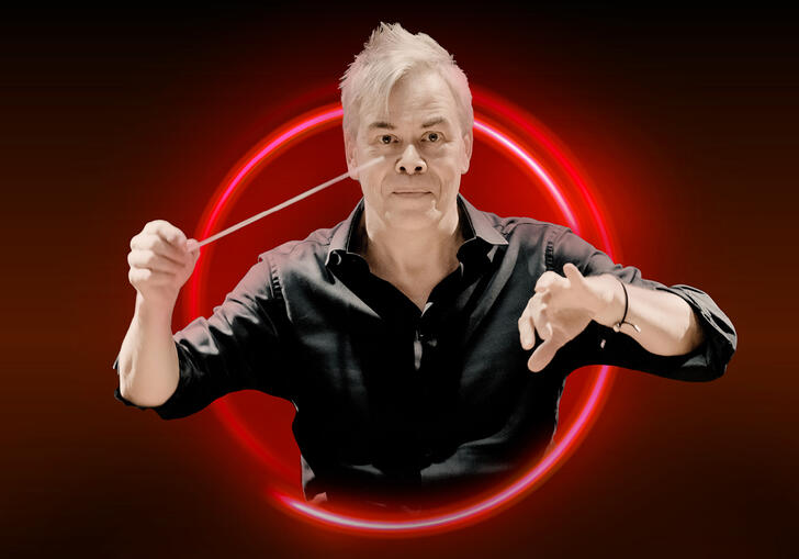 Hannu Lintu with his arms raised against a red bakcground