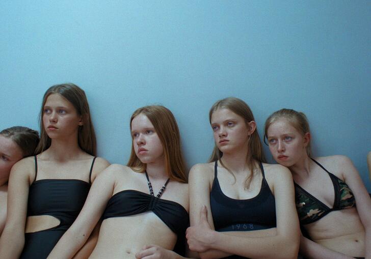 A group of young girls wearing black swimming costumes stare despondently