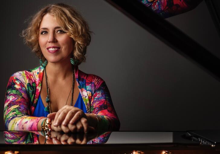 Gabriela Montero wearing a colourful dress sitting by a piano