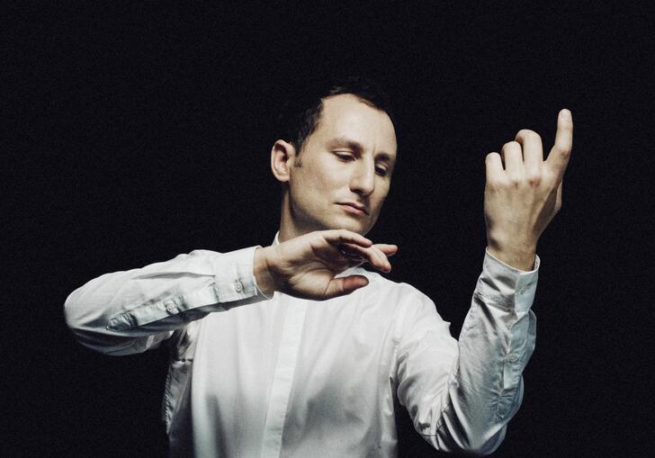 Violist Antoine Tamestit in front of a black background imitating playing his instrument without the actual instrument being there. His eyes are closed.