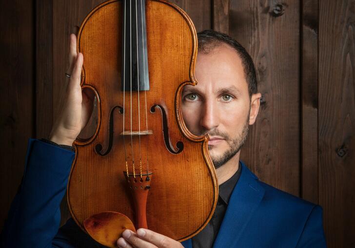 Antoine Tamestit facing the camera, holding a viola upright and facing forwards, in front of the side of his face
