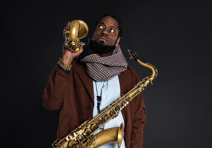 Soweto Kinch against a dark background, holding two saxophones