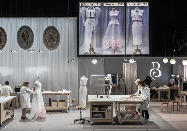 Image of a set with tables and mirrors where people are working together to create a dress