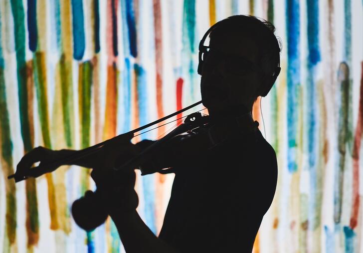 A silhouette of a violinist in front of a multi colour background