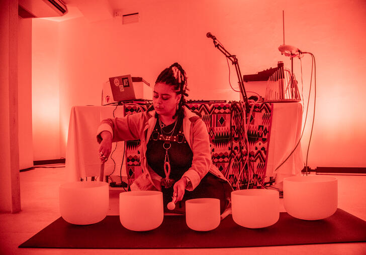 Hannah Catherine Jones sits in a room lit by an orange light playing bowl-shaped objects.