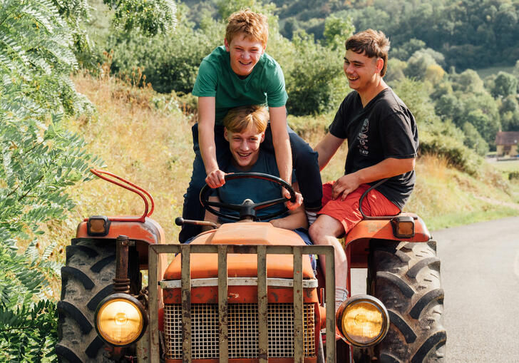 Three teenagers ride on top of a red tractor, grinning