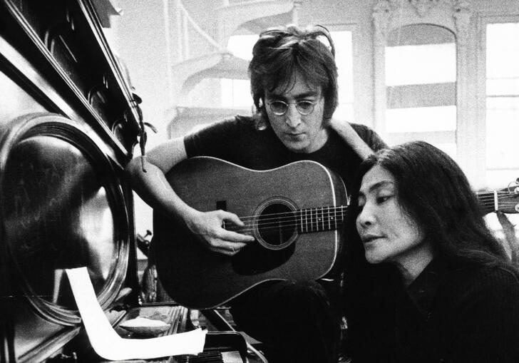 John Lennon and Yoko Ono sit in front of a piano, looking at sheet music