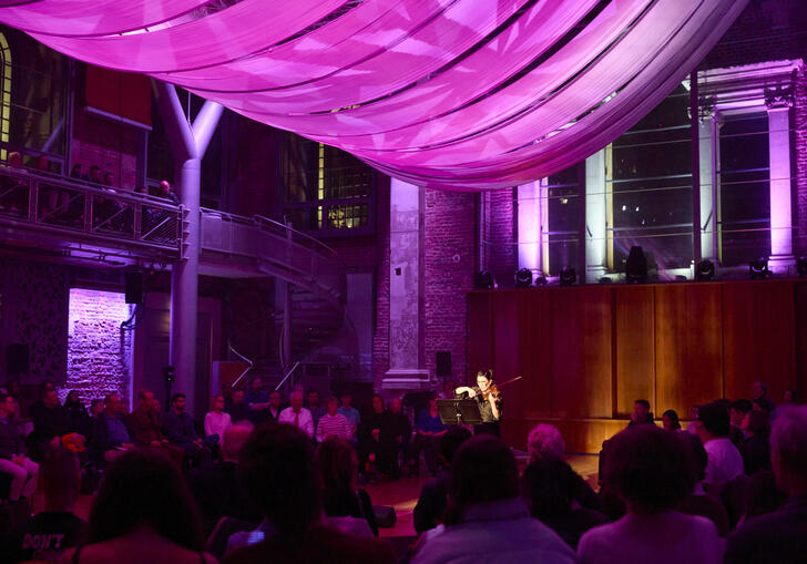 Violinist performs at LSO St Luke's under a drape with purple projections on it