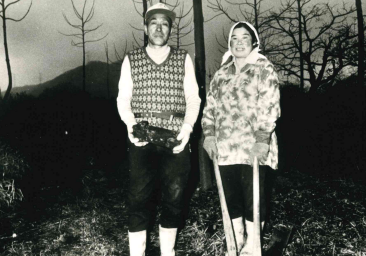 Two people smile at the camera, waring outdoor clothing in a black and white photograph
