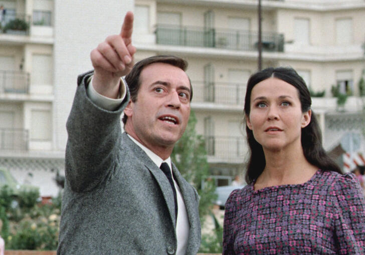 A male-presenting character stands on the left, pointing at something ahead of them. A woman stands on the right, her gaze following his finger.