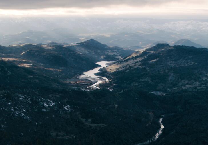A mountainous landscape, with a reservoir and dam in the foreground and a river winding through the hills beyond.