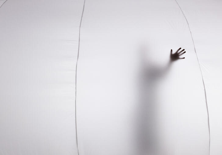 The silhouette of a person can be seen from inside a bubble, their hand is pressed against the material.