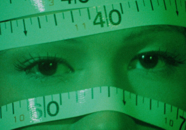 A person's head wrapped in tape measures, bathed in green light