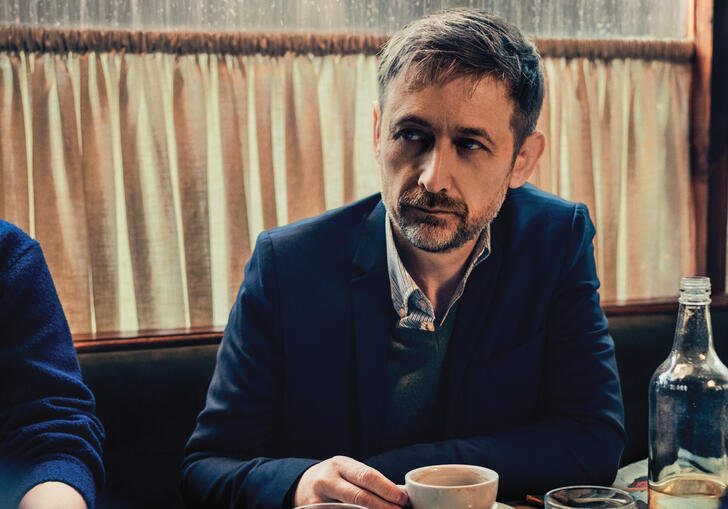 Neil Hannon sitting at a table drinking coffee