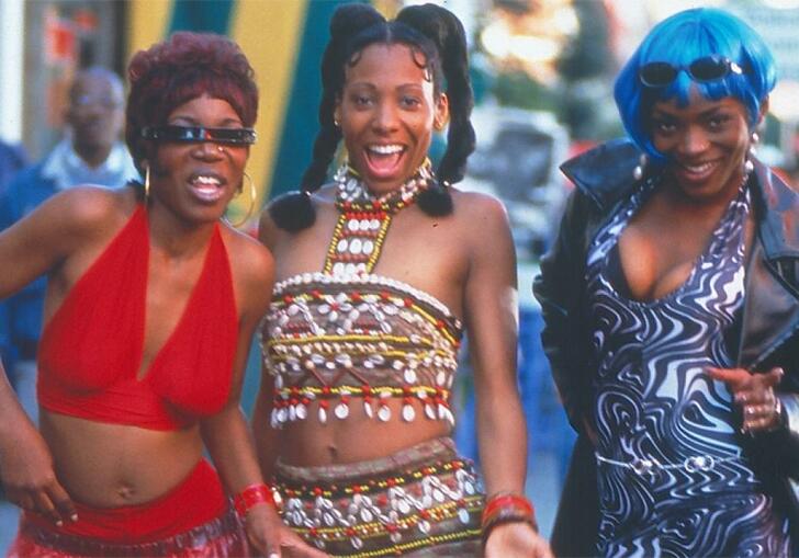 Three Black women standing in a row and smiling, wearing colourful clothes 