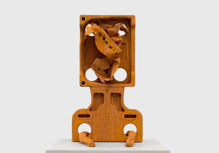 A cast iron sculpture that loosely resembles a head and shoulders, with a twisted form in the head cavity.
