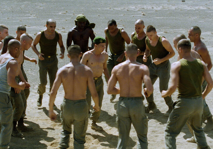 Shirtless men stand in a circle ready to fight