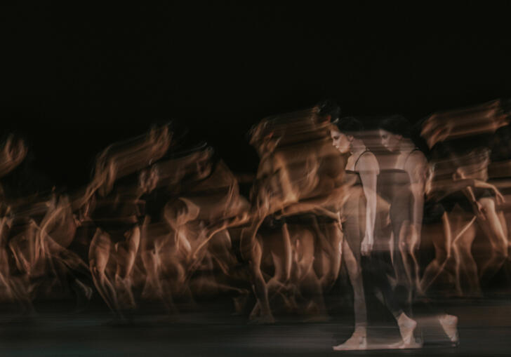 Blurry image of multiple dancers in dark costumes