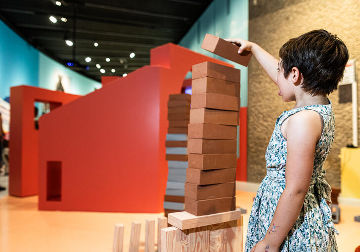 A small child plays jenga, they reach to put a block on the top.