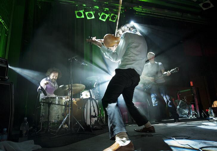 Image of a band perfoming with the guitarist's back to the camera and drummer in the background