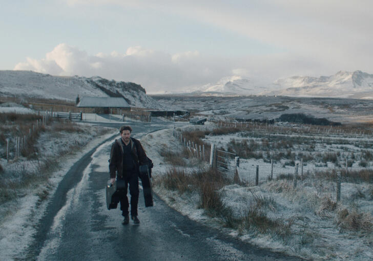 A man walks down a snowy path, holding lots of luggage