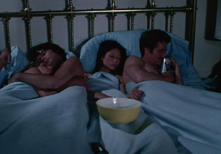 Two couples lie in bed together.